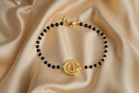 Om Gold bracelet with black beads on a beige fabric background
