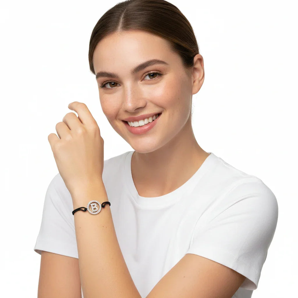 Woman wearing silver diamond alphabet B bracelet with black cord, smiling, white top