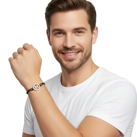 Man wearing a silver diamond H initial bracelet with black cord on white background