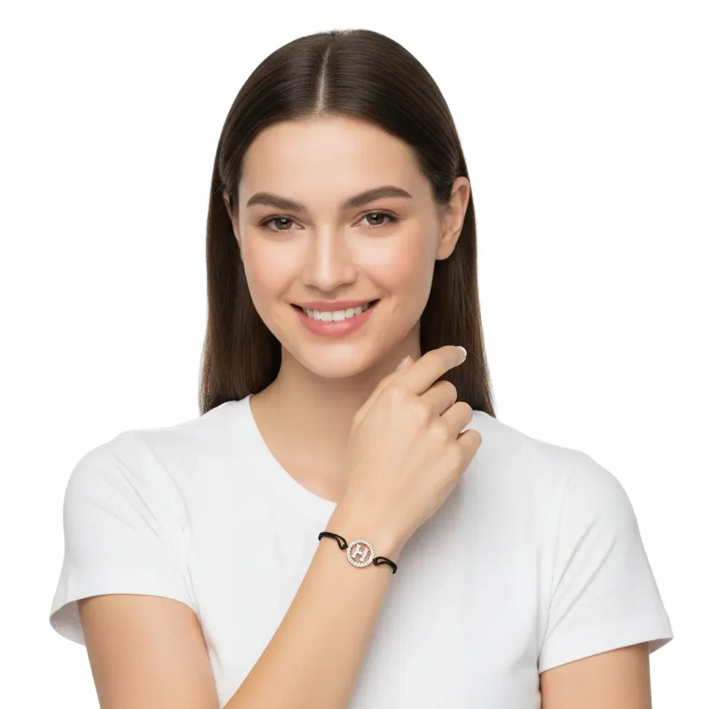 Woman wearing a silver diamond H initial bracelet on black cord, minimalist jewelry style