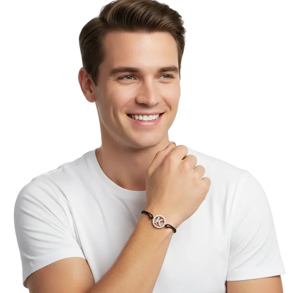 Man wearing a silver diamond K alphabet bracelet on a black cord, white background